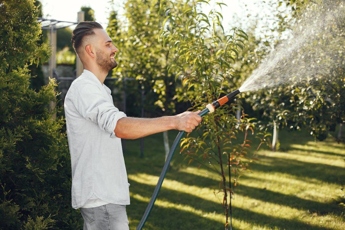 A person watering plants in a garden, showing proper lawn care and outdoor maintenance practices