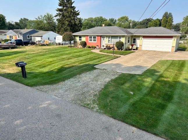 A mowed front yard with a black mailbox and gravel driveway in front of a ranch-style house.